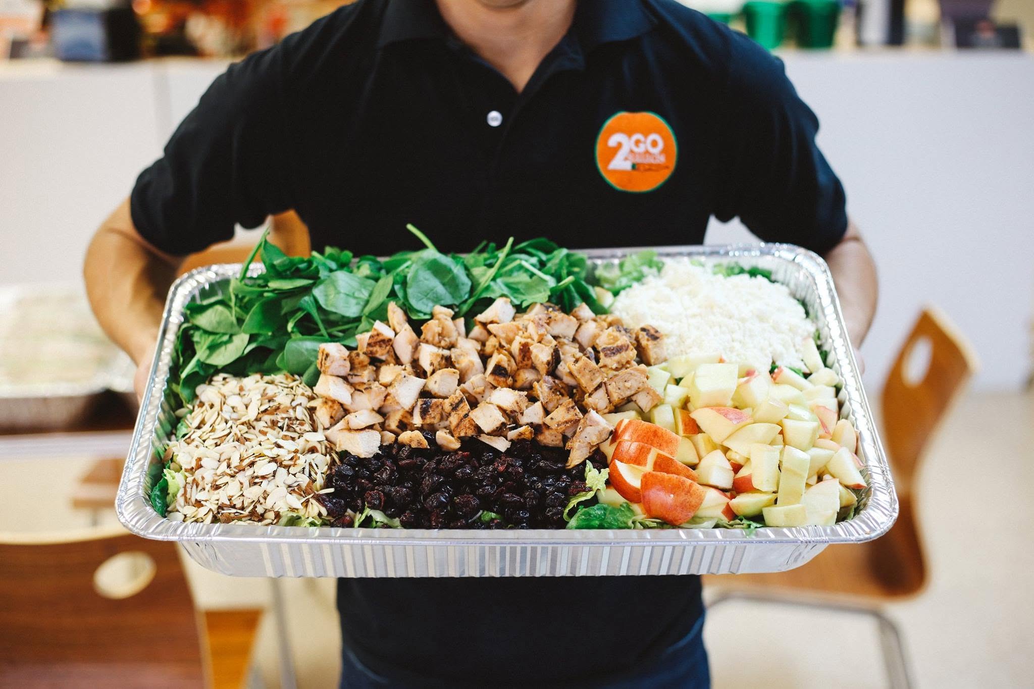2GO Salads team member holding a catering tray of Apple Chicken Salad